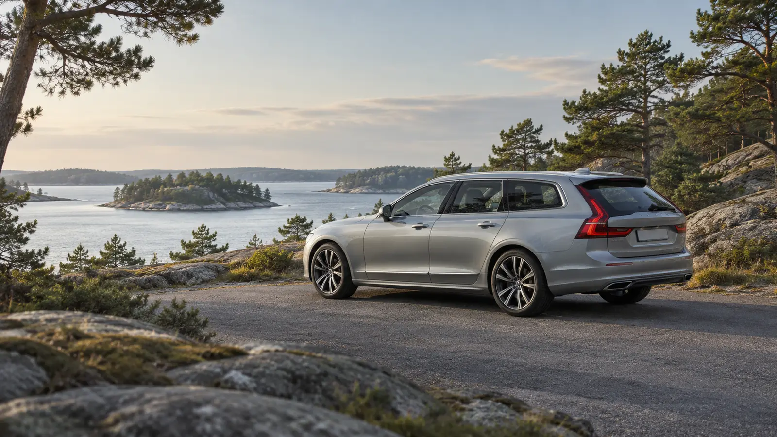 Silverfärgad kombi på en grusplan bland klipphällar och tallar, med utsikt över skärgården