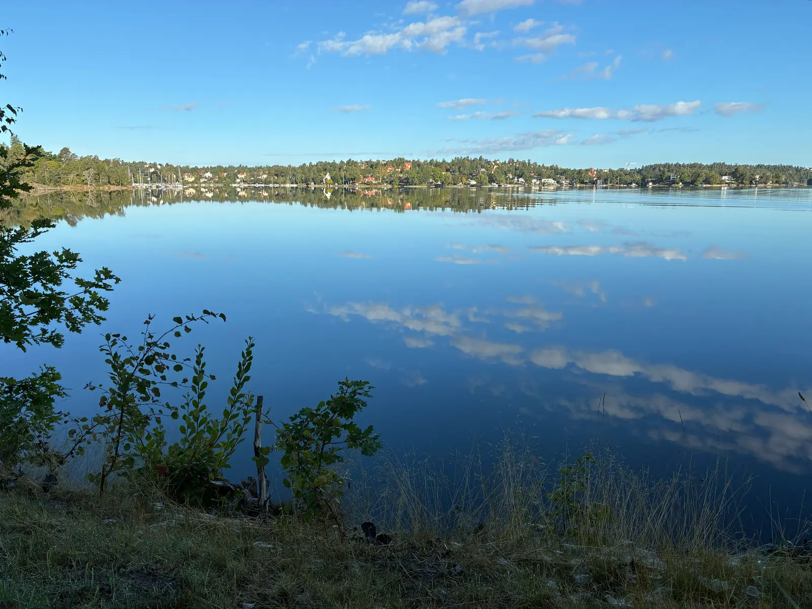 Stilla vik en klar morgon, villor och båtar längs stranden speglas i vattnet